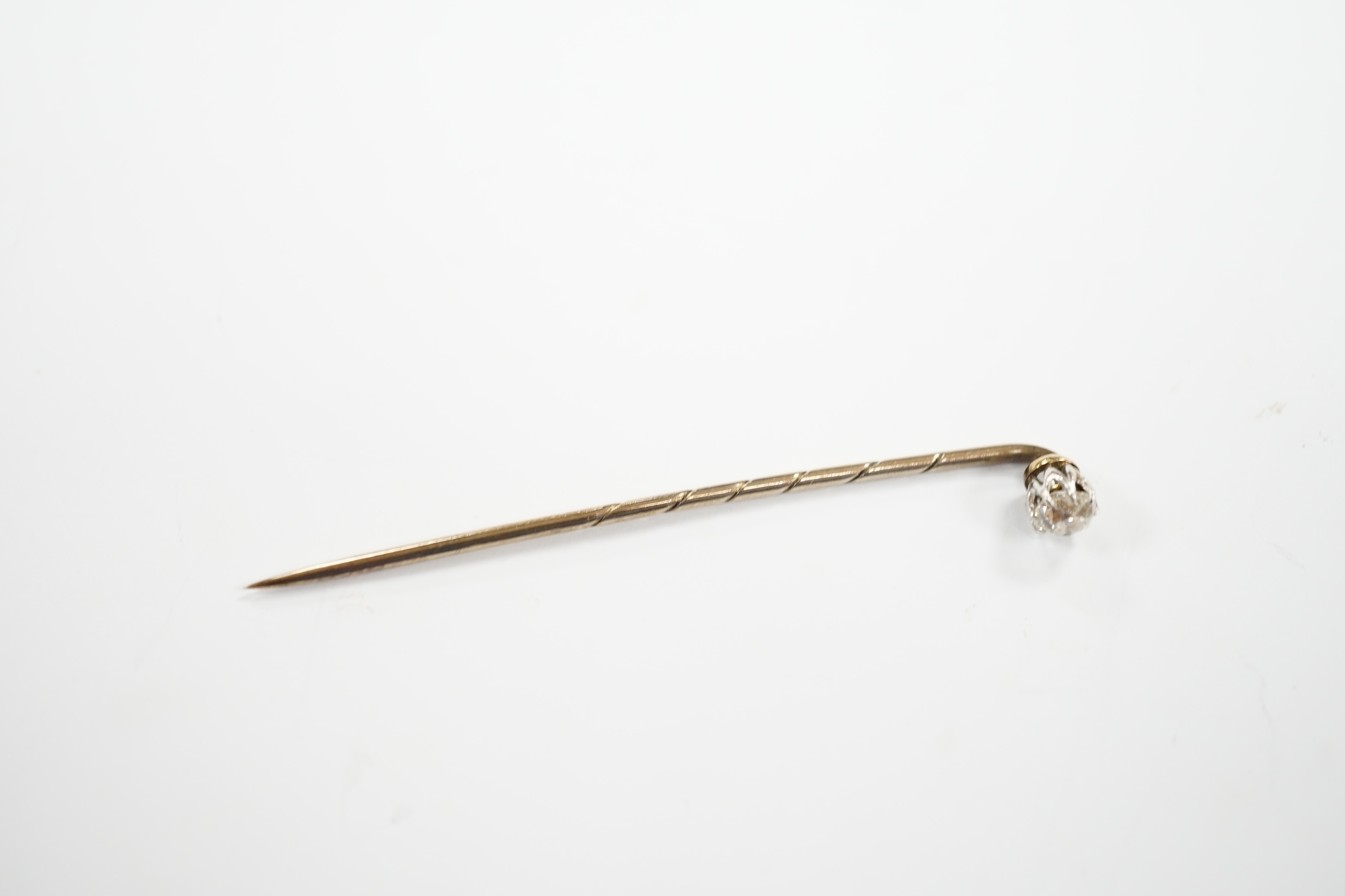 An early 20th century cased yellow metal and cushion cut solitaire diamond set stick pin, 57mm, gross weight 1.3 grams.